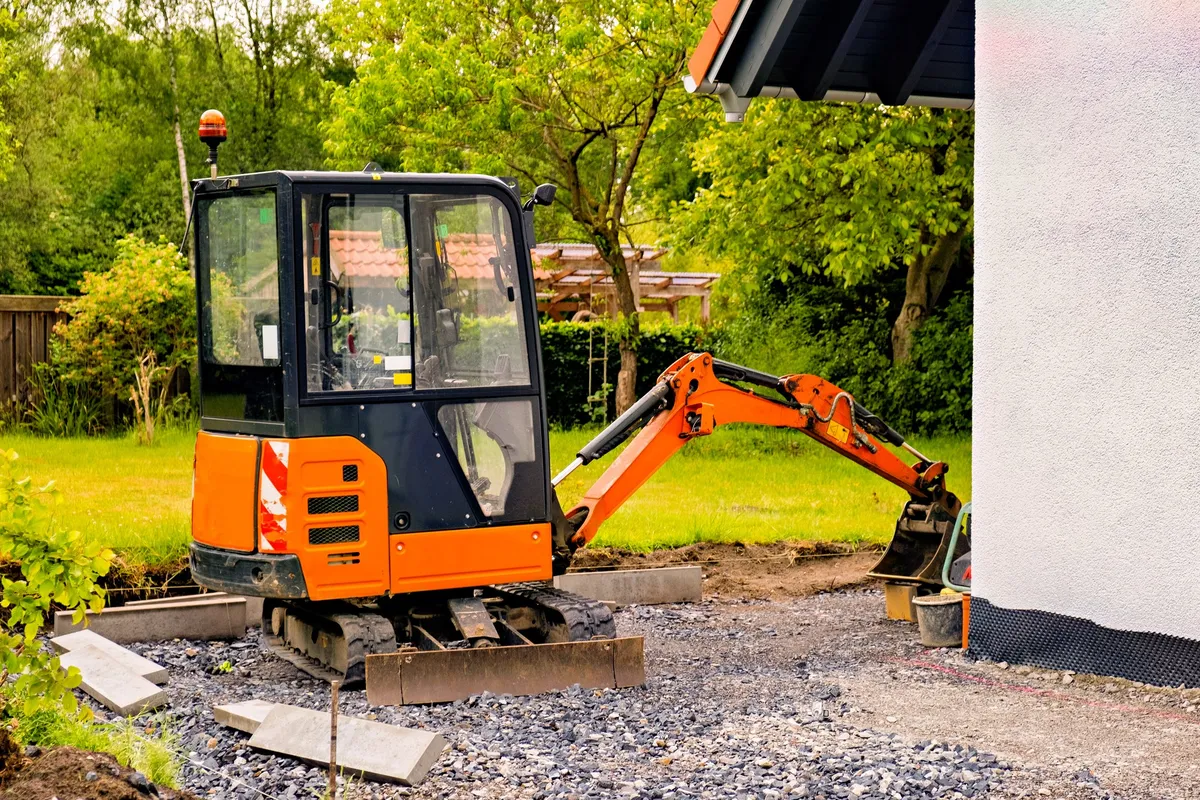 Top Compact & Mini Excavator Diggers- TYPHON Machinery A small orange excavator near a private home, illustrating the compact and eco-friendly options in construction.