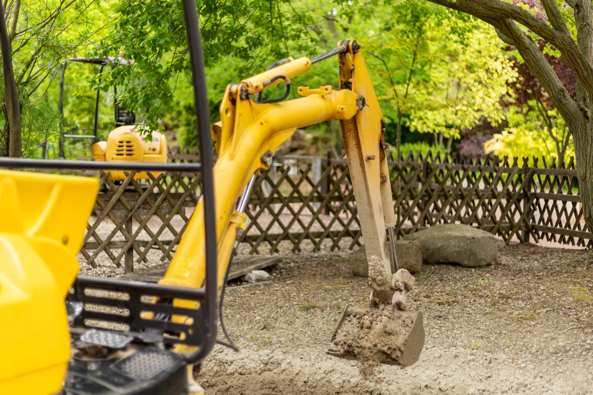 Top Compact & Mini Excavator Diggers- TYPHON Machinery A yellow mini excavator digs into soil at a construction site, illustrating its use for small projects.